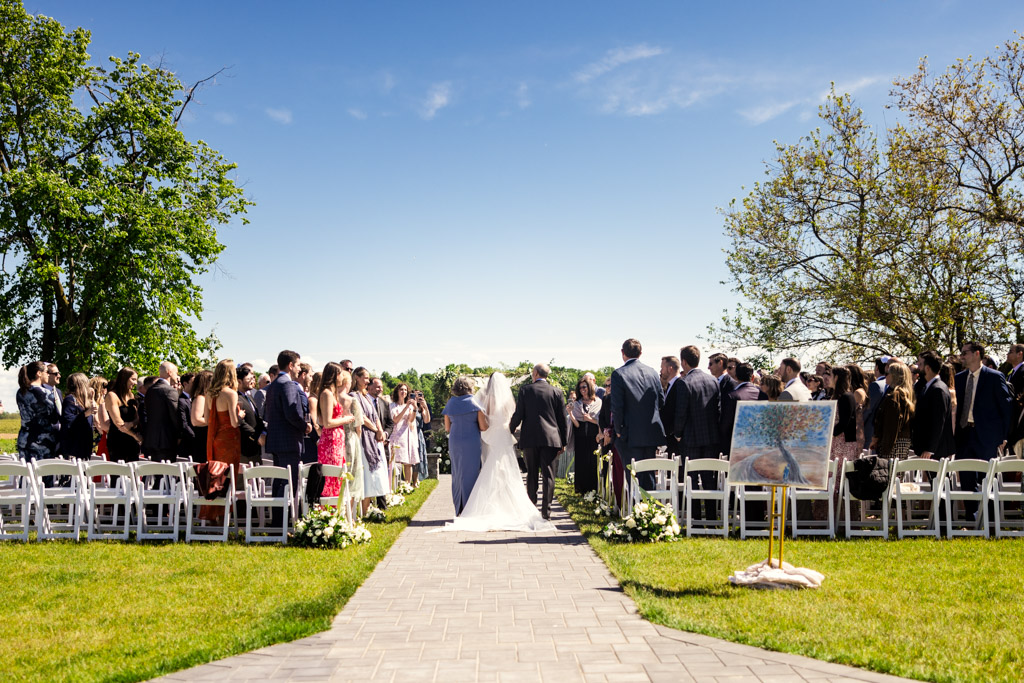 Bride walking down the outdoor aisle at Être Farms, with guests standing on either side under a sunny blue sky