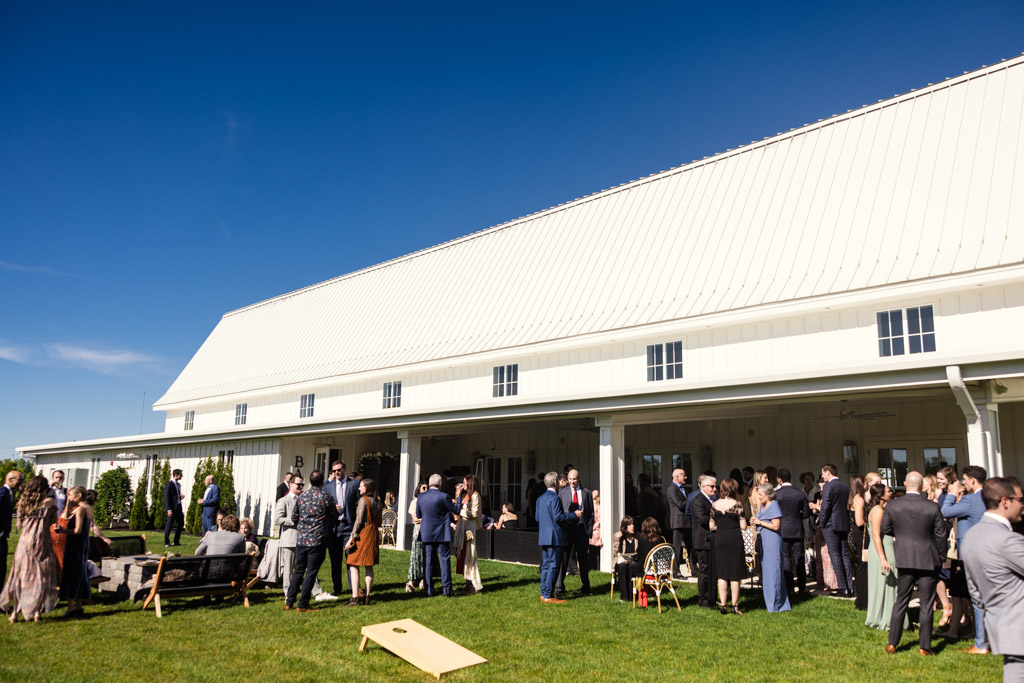 Guests during cocktail hour outside the large white barn at Être Farms on a sunny day