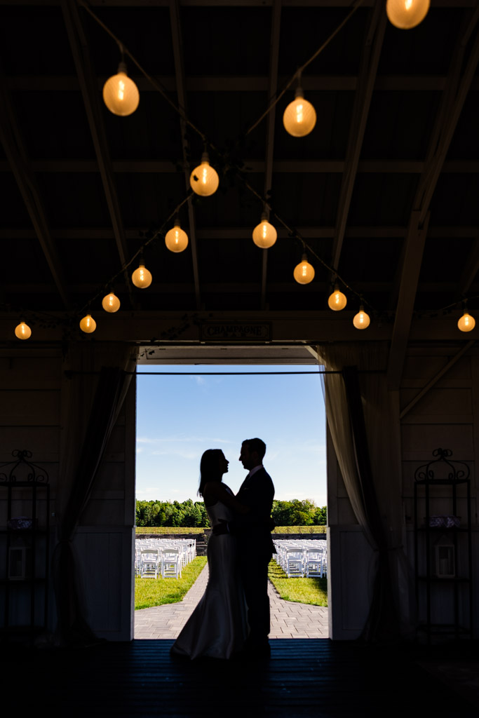 Silhouetted newlywed couple stands in a doorway at Être Farms under string lights, with outdoor chairs and lush greenery visible outside