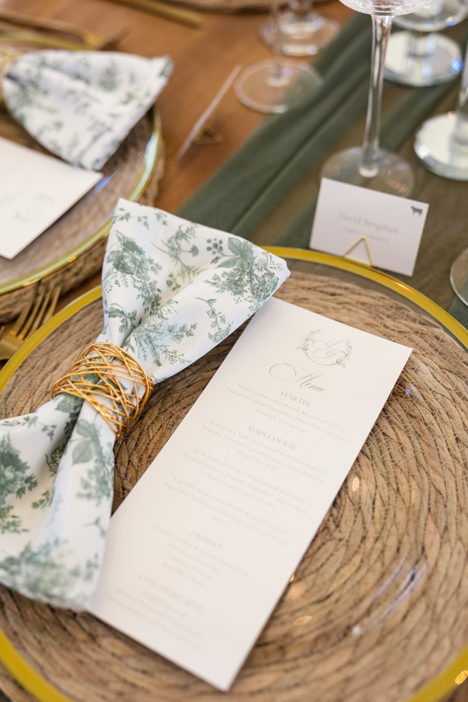 Guest table setting for spring Être Farms wedding reception features a floral napkin, gold napkin ring, and printed menu on a woven placemat