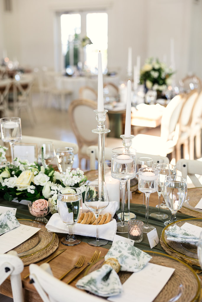 Guest table setting with candlesticks, glassware, white flowers, and napkins in a bright, airy room at Être Farms wedding reception space