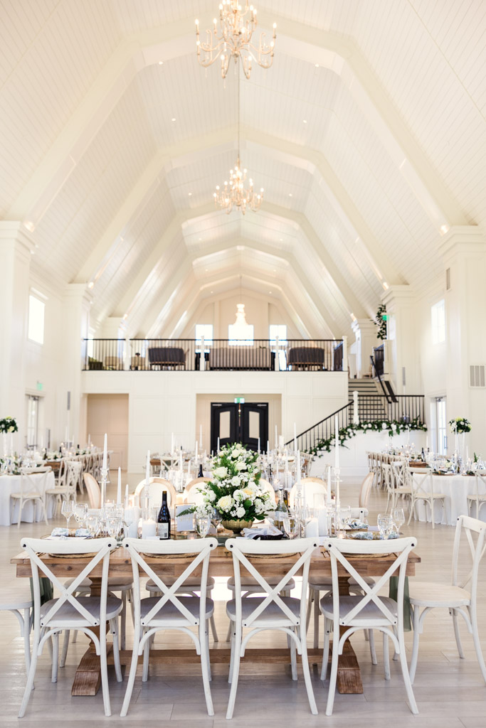 Wedding reception hall at Être Farms with white decor, floral centerpieces, and chandeliers under a high vaulted ceiling