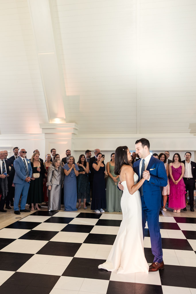 Bride and groom share their first dance on a black-and-white checkered floor at Être Farms as wedding guests watch and smile