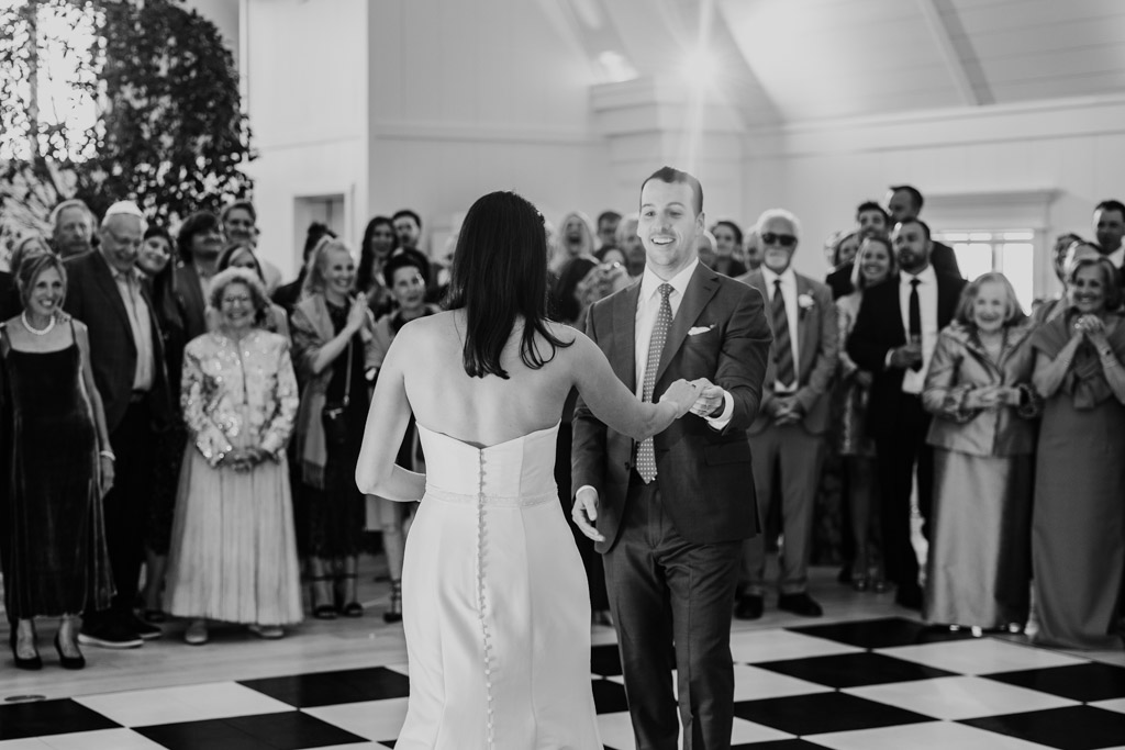 Black and white photo of newlywed couple during their first dance at their Être Farms wedding reception while guests watch and smile in the background
