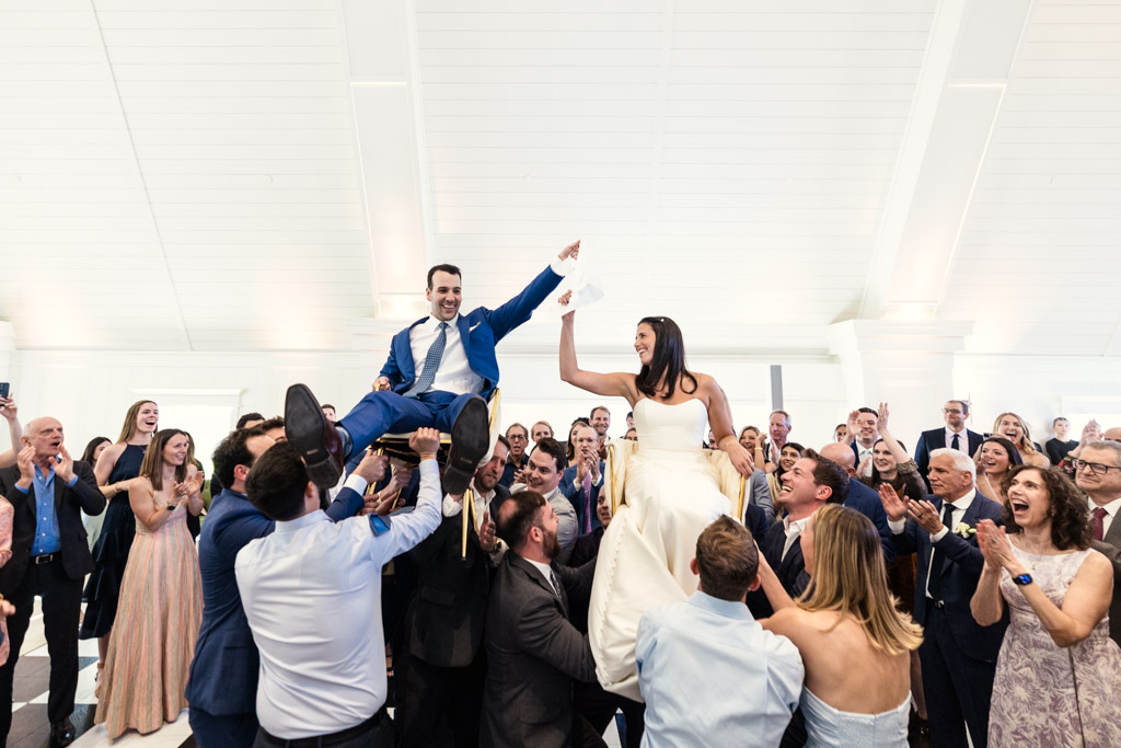 Bride and groom lifted on chairs during the hora at their Être Farms wedding celebration, surrounded by cheering guests