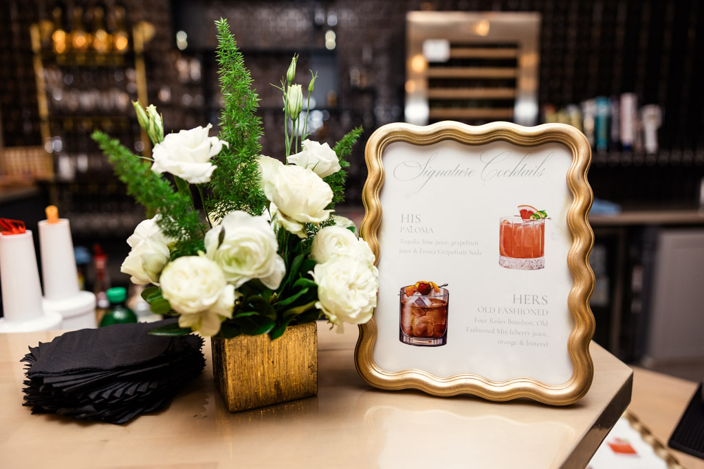 Gold-framed custom cocktail menu with white flowers in a gold vase on the Être Farms bar counter