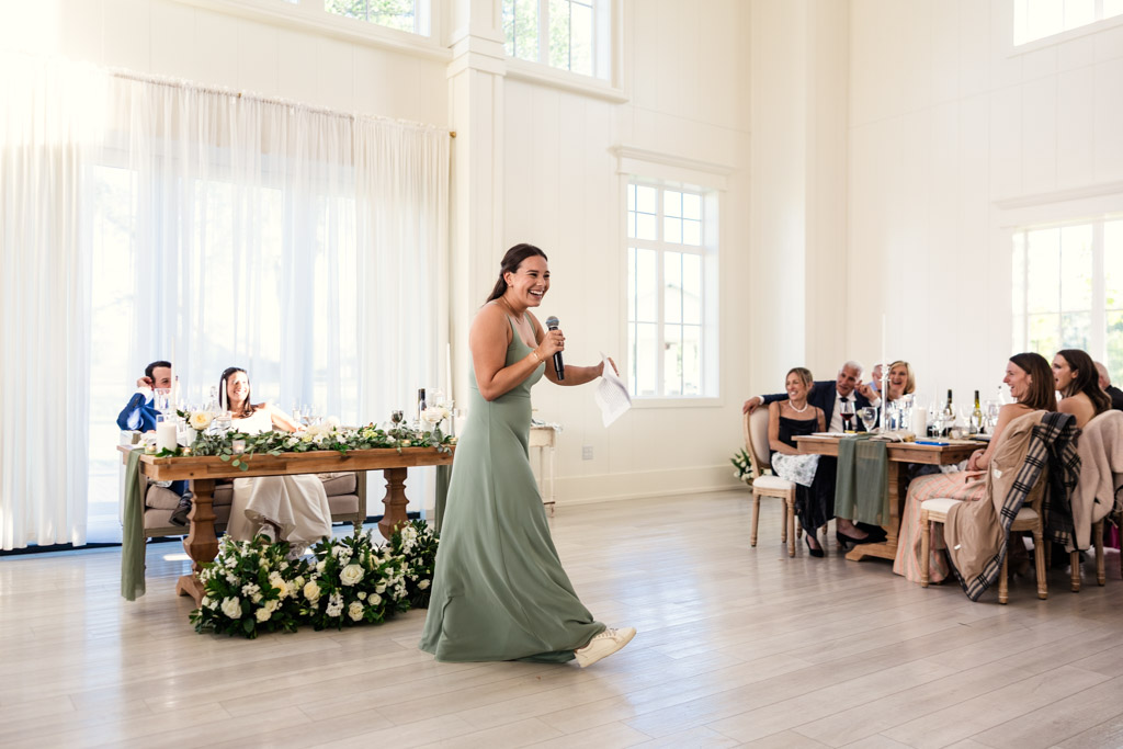 Maid of Honor in a green dress gives a speech at an Être Farms wedding reception, smiling at the seated guests