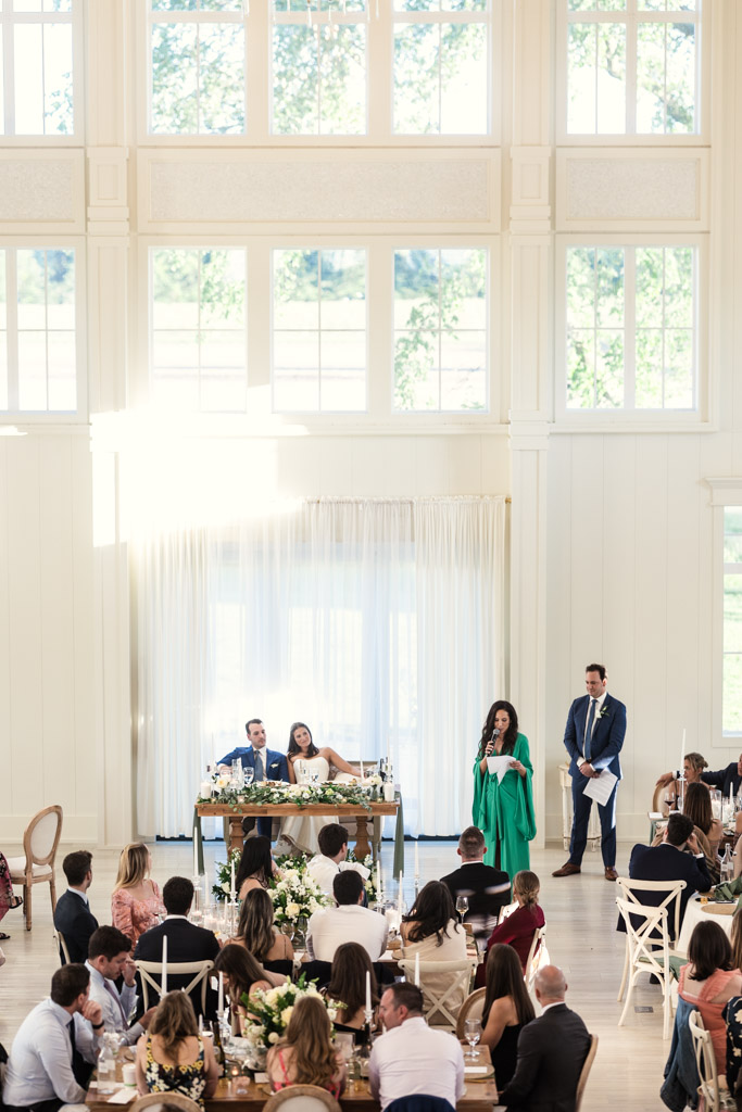 Groom's sister gives speech at a wedding reception in Être Farms’ bright reception hall with large windows