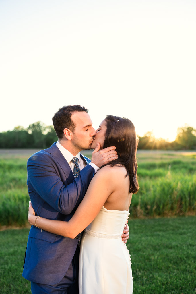 Bride and groom kiss outdoors at sunset at Être Farms, surrounded by lush green fields