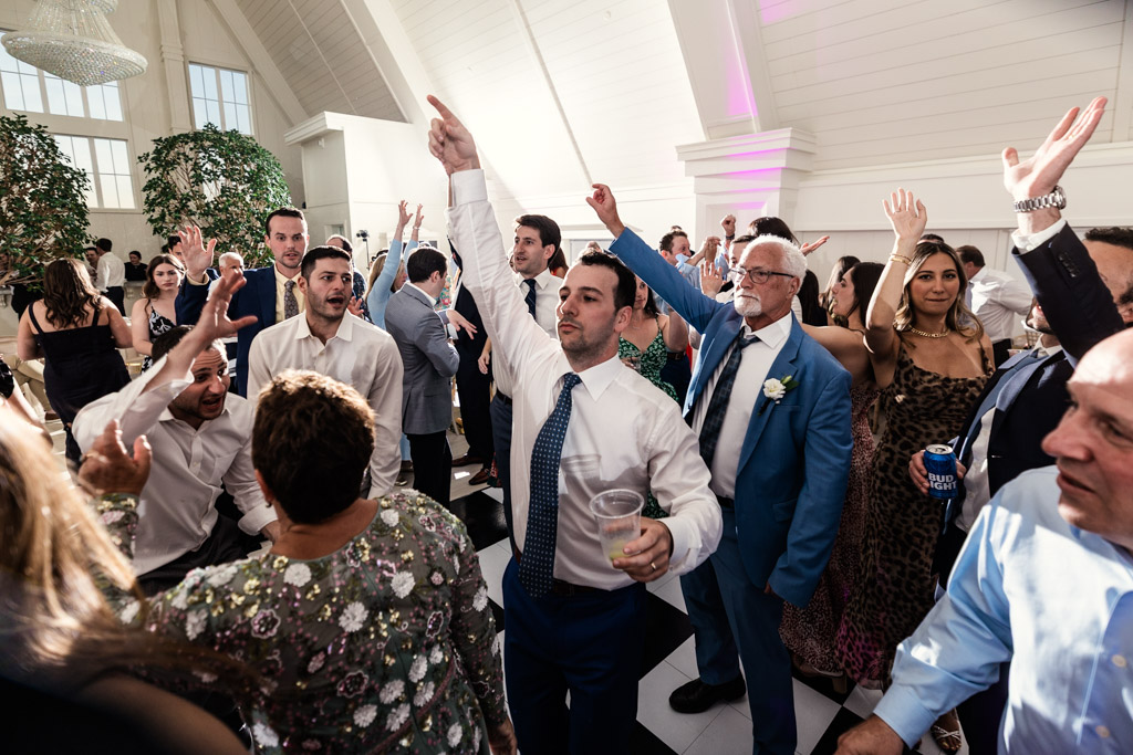 Guests dancing and raising their hands at a lively Être Farms indoor wedding reception, surrounded by white walls and bright lighting