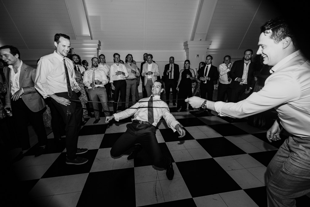Black and white photo of groom doing the limbo at Être Farms wedding reception as others watch and smile on a black and white checkered floor