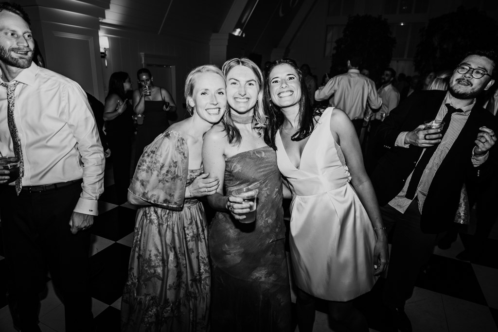 Black and white photo of bride and two guests on the dance floor at an Être Farms wedding reception surrounded by other guests