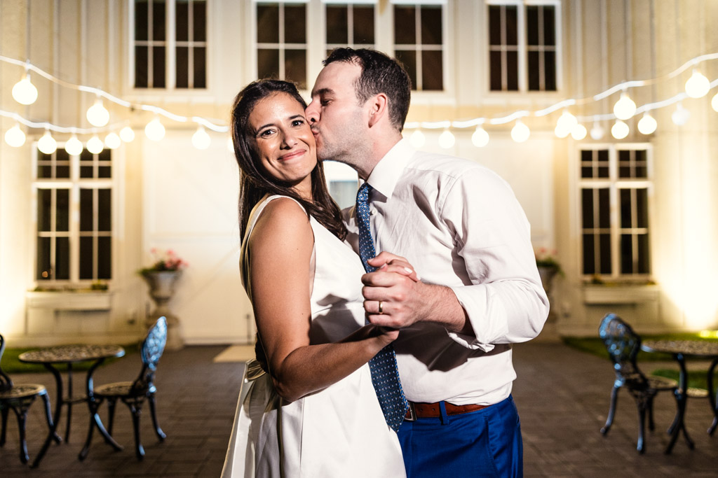 Groom kisses bride on the cheek as they dance outdoors under string lights at night during their Être Farms wedding reception