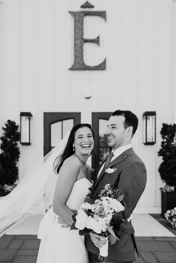 Black adn white photo of bride and groom laughing and embracing outside Être Farms main entrance