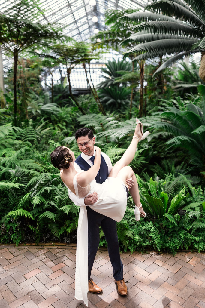 Man lifts his smiling partner inside the Fern Room during their Garfield Park Conservatory engagement session