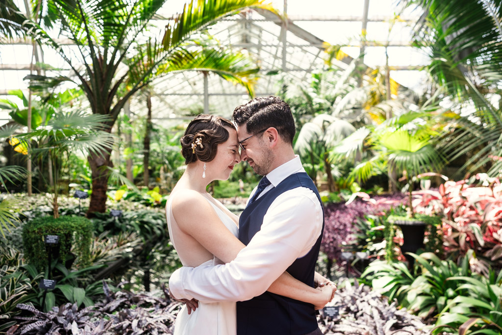 Couple holds each other standing forehead to forehead surrounded by lush plants during their engagement session at Garfield Park Conservatory