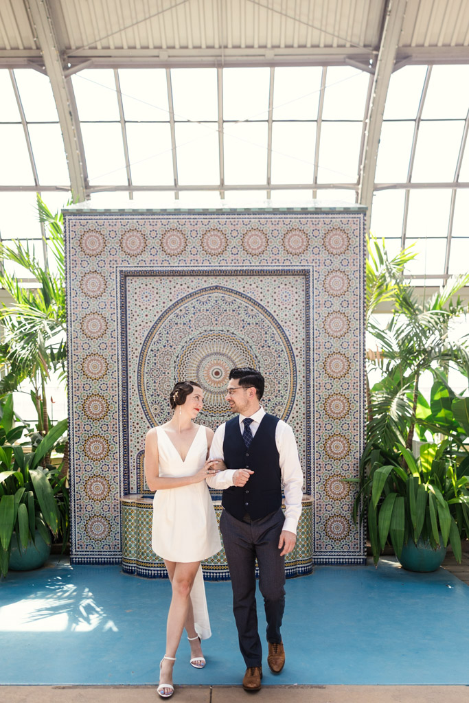 A couple dressed formally smiles at each other, standing arm in arm in front of Zellij Fountain during their Garfield Park Conservatory engagement session