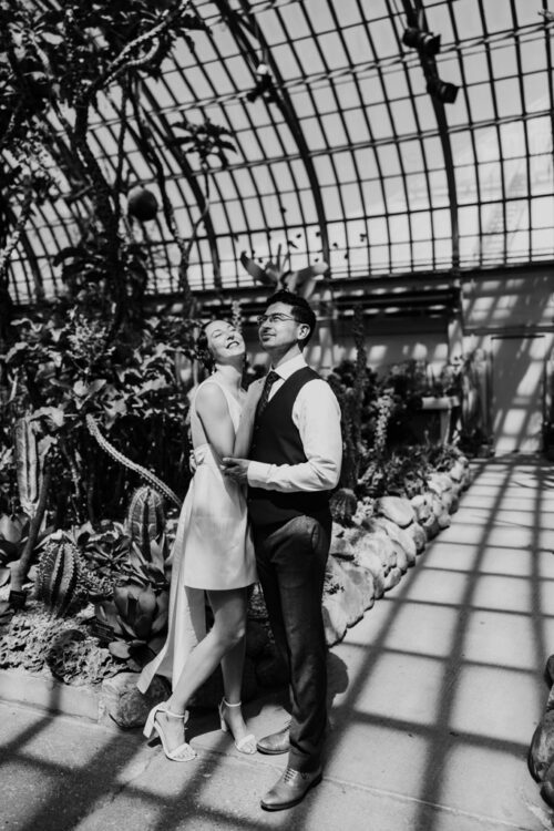 Black and white photo of engaged couple smiling and posing in a sunlit greenhouse at Garfield Park Conservatory in Chicago