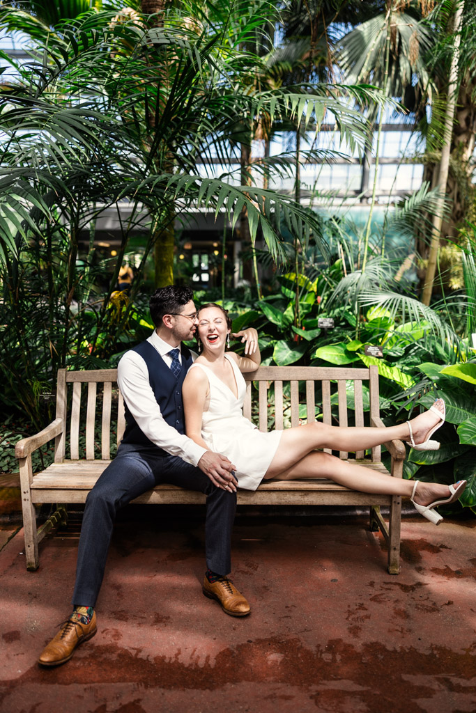 Happy engaged couple sits on a bench surrounded by lush plants inside Garfield Park Conservatory