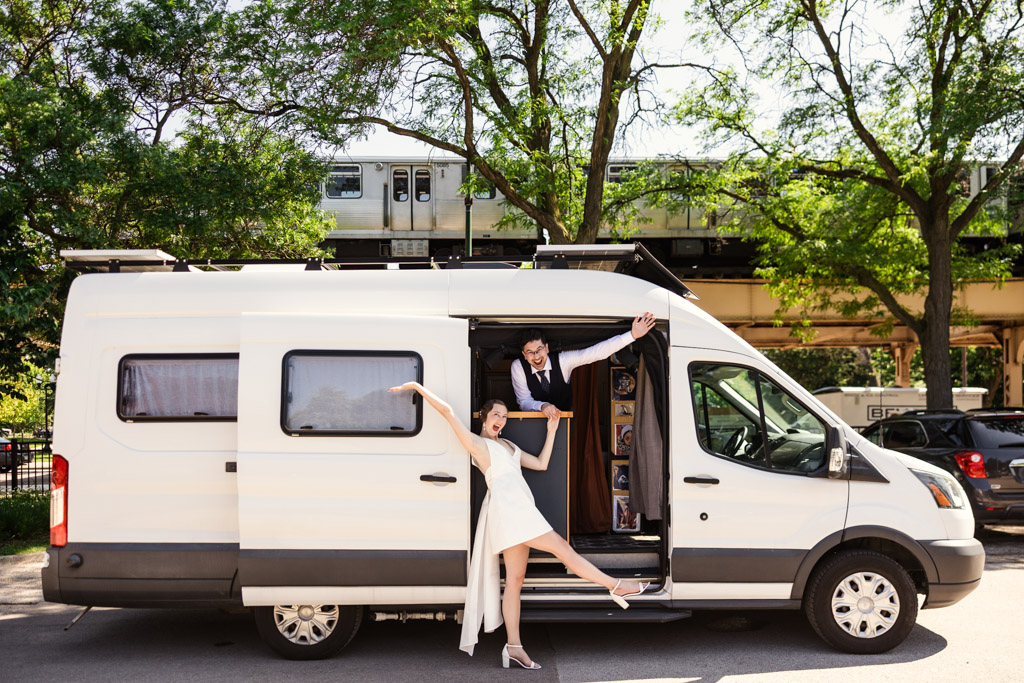 Happy engaged couple poses with their camper van at Garfield Park Conservatory with a CTA train passing on elevated tracks behind them