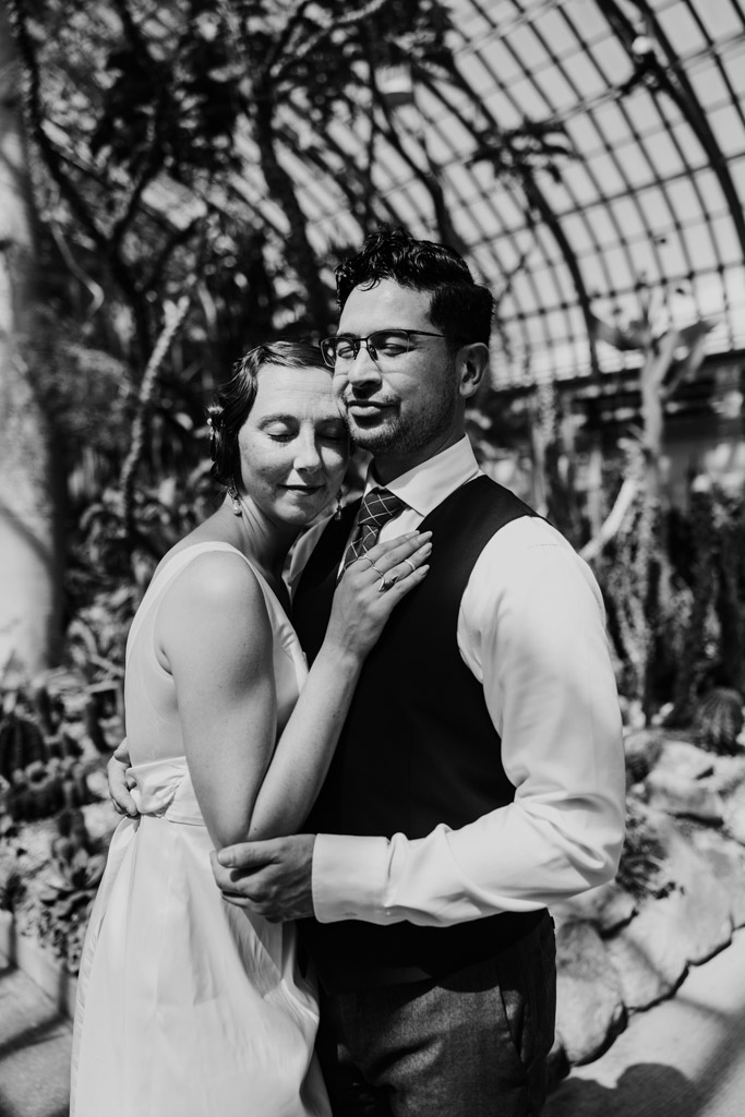 Black and white photo of engaged couple embracing in a sunlit room at Garfield Park Conservatory
