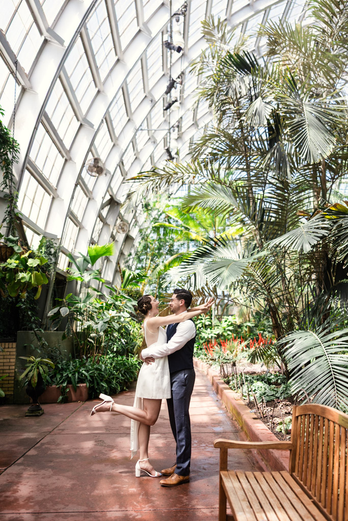 Engaged couple embraces and smiles in a lush indoor botanical garden at the Garfield Park Conservatory
