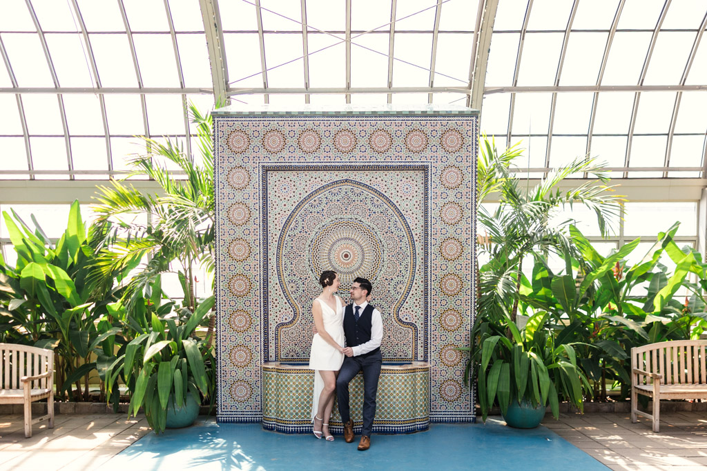 Romantic engagement photo at Garfield Park Conservatory of couple sitting in front of Zellij Fountain in Garfield Park Conservatory surrounded by greenery