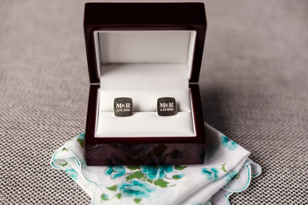 Square engraved cufflinks in a box rest on a floral handkerchief before wedding celebration at Kemper Lakes Golf Club