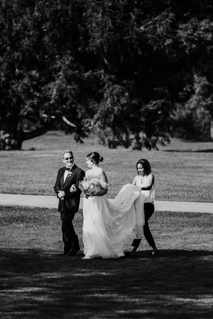 Black and white photo of bride with a bouquet walking outdoors with her father during wedding ceremony at Kemper Lakes Golf Club