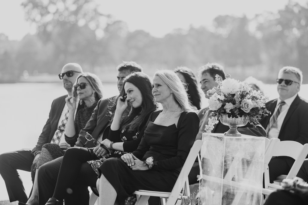 Black adn white photo of guests sitting on white chairs outdoors at Kemper Lakes Golf Club wedding ceremony