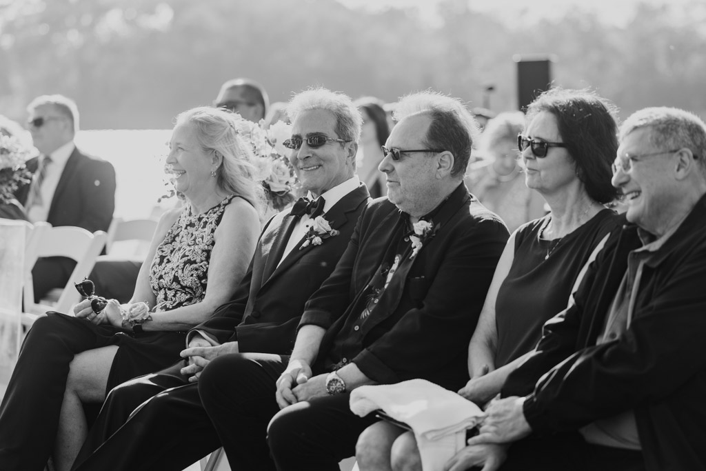 Black and white photo of bride's parents and other guests sitting in a row outdoors at Kemper Lakes Golf Club wedding ceremony
