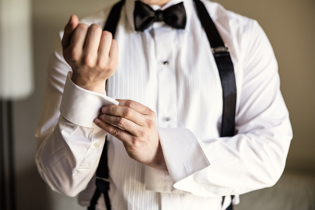 Groom adjusts his shirt cuff, wearing suspenders and a bow tie while getting ready for his wedding at Kemper Lakes Golf Club