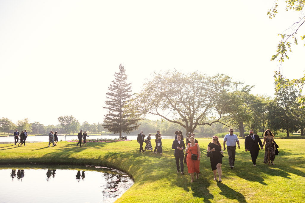 Guests dressed formally walk on grass near a pond at Kemper Lakes Golf Club