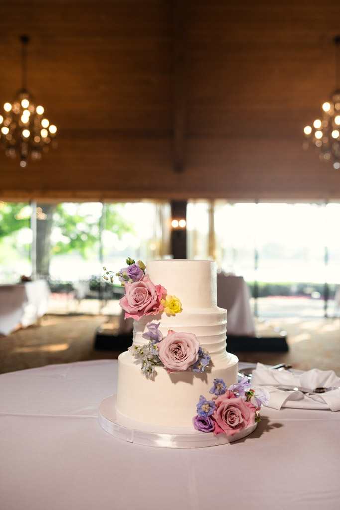 Three-tier white wedding cake decorated with pink and purple flowers on a table for wedding reception at Kemper Lakes Golf Club