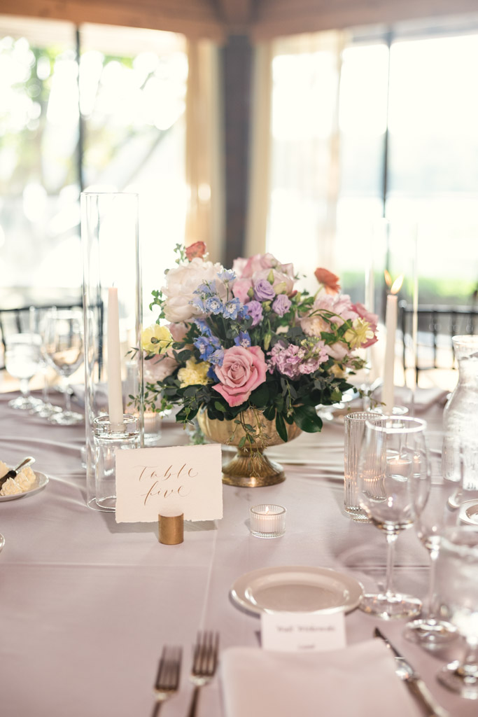 Guest table setting with pastel flower centerpiece, candles, glassware, table marker for Kemper Lakes Golf Club wedding reception