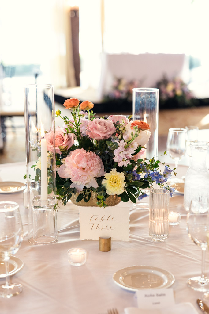 Floral centerpiece with pink and yellow flowers, candles, and table marker on a white tablecloth for Kemper Lakes Golf Club wedding reception