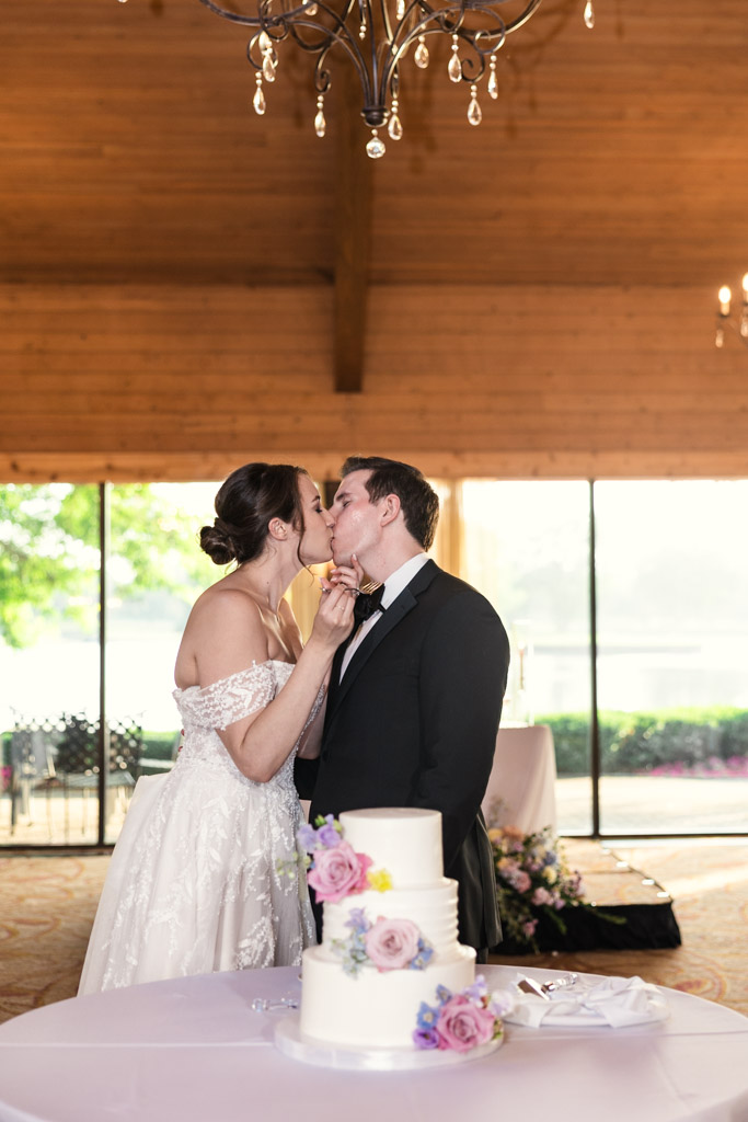 Bride and groom kiss after cutting their wedding cake at their Kemper Lakes Golf Club reception