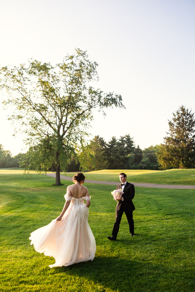 Bride and groom walk on a sunny green lawn at Kemper Lakes Golf Club, with trees in the background and golden hour light