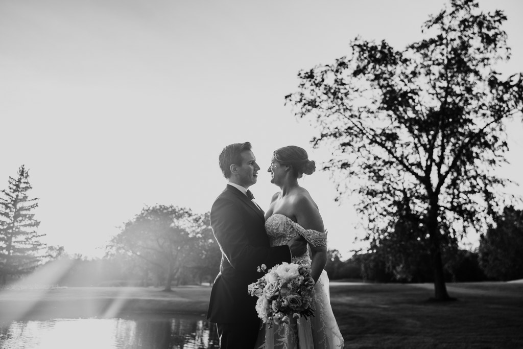 Black and white photo of bride and groom standing together outdoors at sunset at Kemper Lakes Golf Club