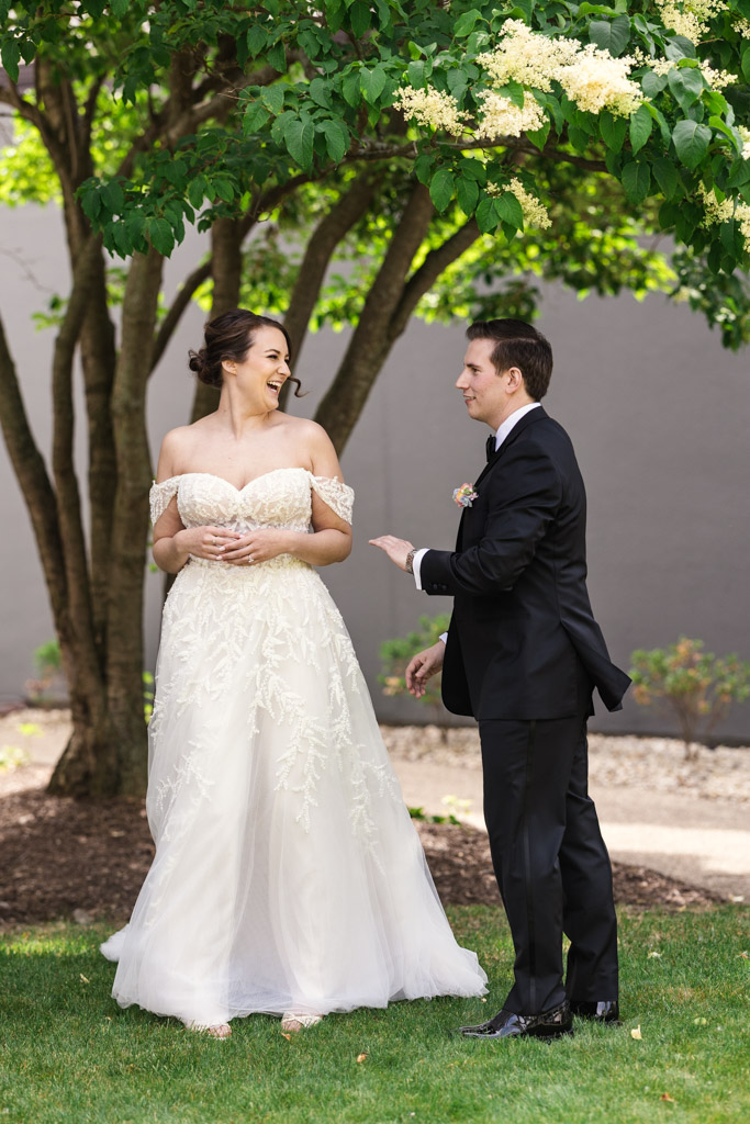 Bride and groom smiling and laughing together under a tree during their first look before their wedding at Kemper Lakes Golf Club