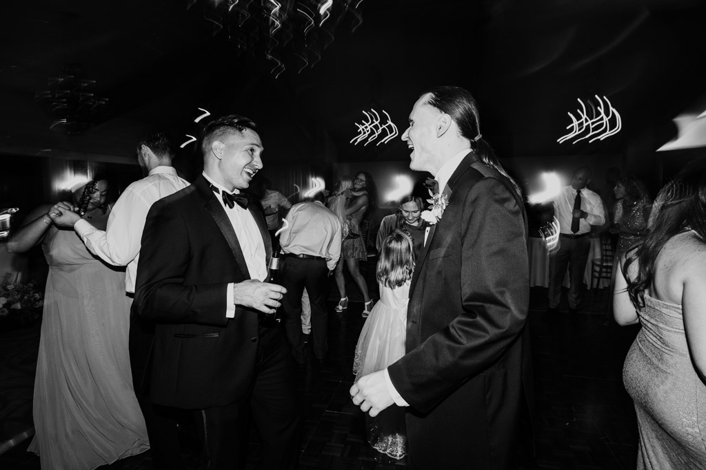 Black and white photo of groomsmen laughingon the dance floor during wedding reception at Kemper Lakes Golf Club surrounded by other guests