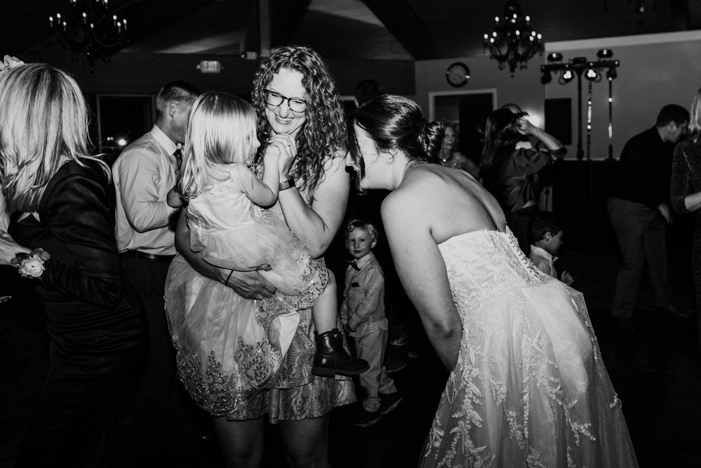 Black and white photo of bride smiles at a woman holding a young girl on the dance floor at Kemper Lakes Golf Club wedding reception