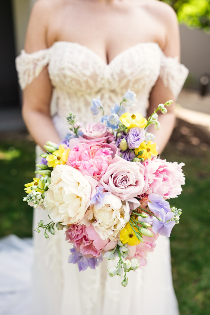Bride in lace off-shoulder gown holding a colorful bouquet of roses, peonies, and assorted flowers before Kemper Lakes Golf Club wedding