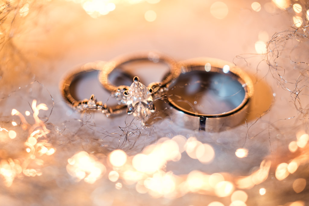 Detail photo of three rings, including a diamond engagement ring, surrounded by warm, sparkling lights during wedding reception at Kemper Lakes Golf Club