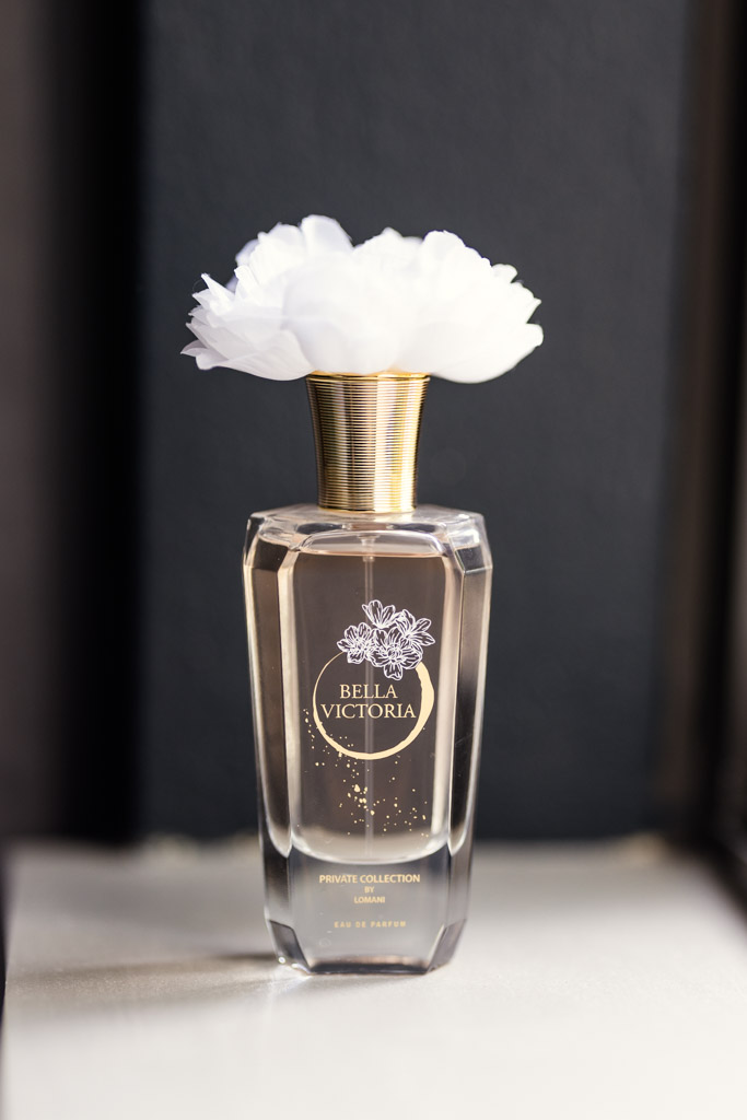 A Bella Victoria perfume bottle with a white flower-shaped cap on a white surface