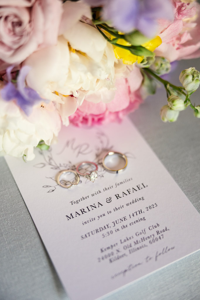 Wedding invitation with three rings on top, surrounded by pastel flowers in pink, white, and yellow hues for Kemper Lakes Golf Club wedding