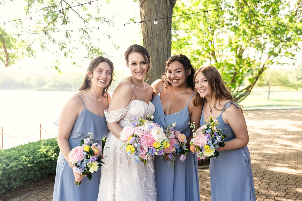 Portrait of bride and bridesmaids holding their bouquets, smiling on a sunny wedding day at Kemper Lakes Golf Club