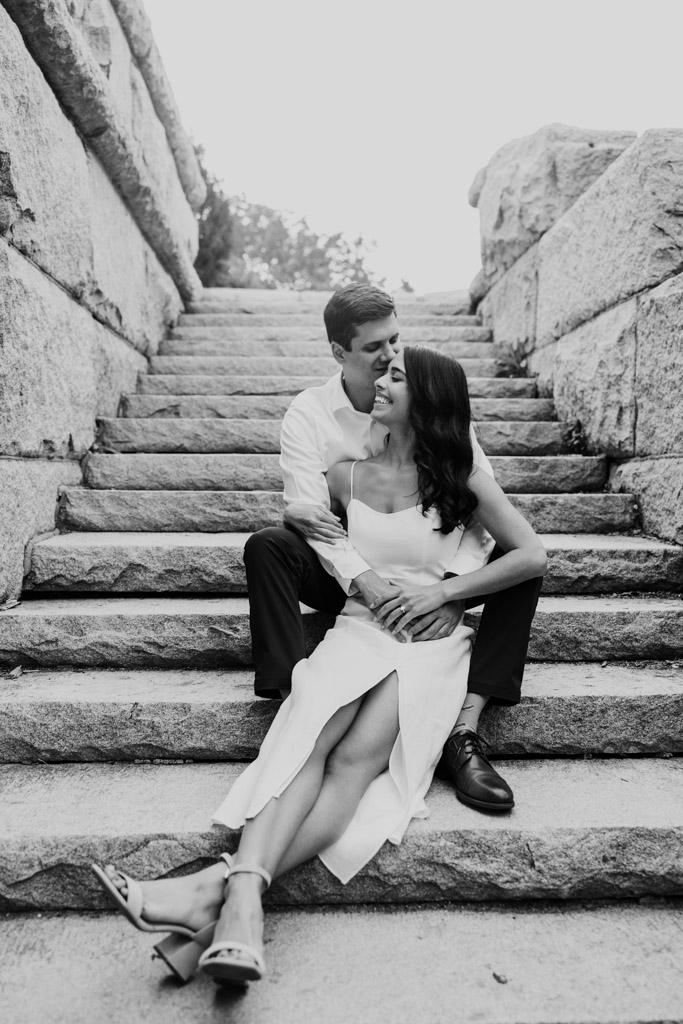 Couple sits on the stone steps of Ulysses S. Grant Mounment in Lincoln Park, embracing and smiling affectionately during spring engagement session