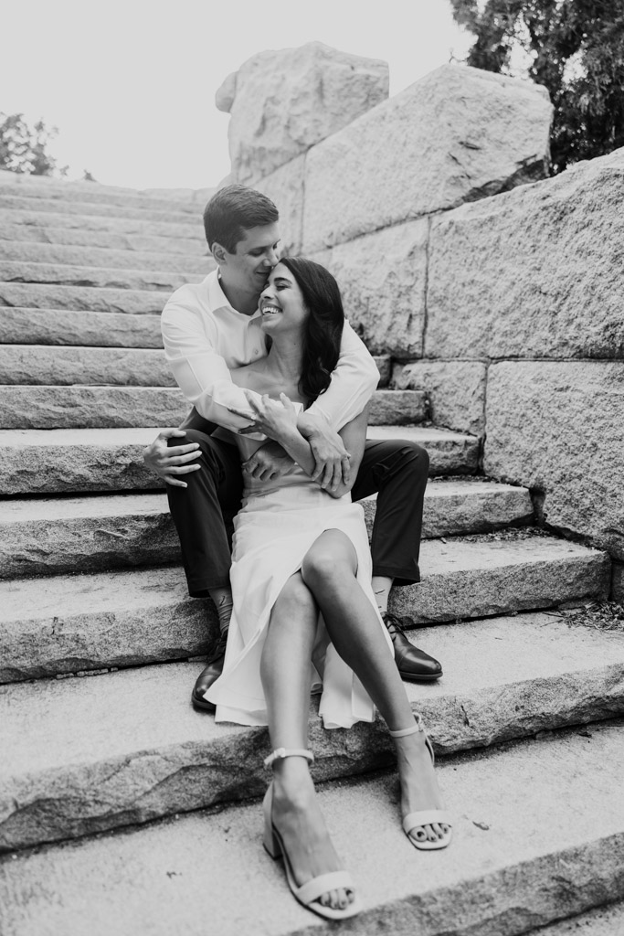 Black and white photo of engaged couple sitting on stone steps at the Ulysses S. Grant Monument in Lincoln Park, smiling and embracing each other