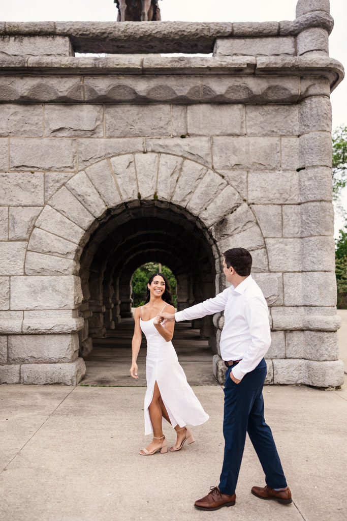 A couple in white outfits walks hand in hand, smiling at each other, in front of a the Ulysses S. Grant Monument in Lincoln Park